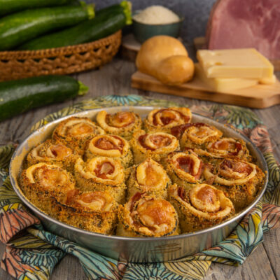Rotolini di zucchine gratinati al forno con prosciutto e formaggio disposti in teglia