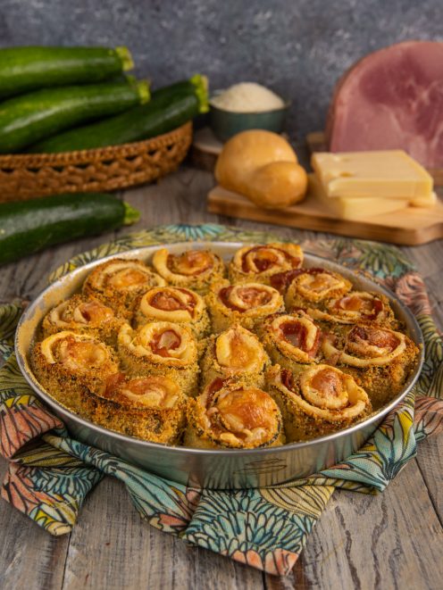 Rotolini di zucchine gratinati al forno con prosciutto e formaggio disposti in teglia