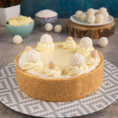 Torta Raffaello con base di frolla, ciuffi di crema al cofano e cocco, decorata con praline e nocciole