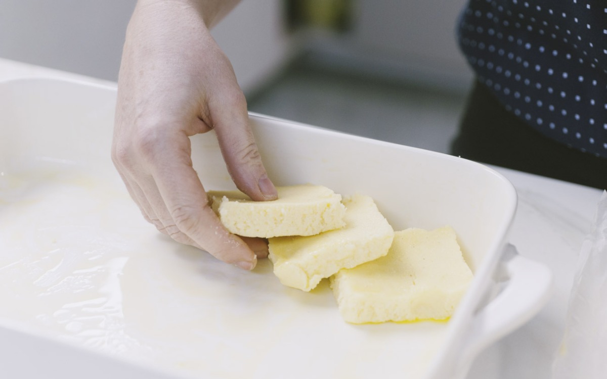 Mano che adagia fette di semolino nella pirofila per completare gli gnocchi alla romana