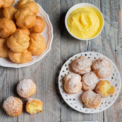 Bignè alla crema spolverati di zucchero a velo, farciti con crema pasticcera e serviti su piatti diversi