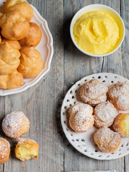 Bignè alla crema spolverati di zucchero a velo, farciti con crema pasticcera e serviti su piatti diversi