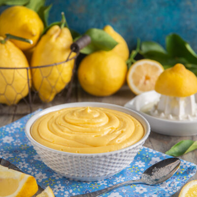 Crema pasticcera al limone vellutata in ciotola, circondata da limoni freschi e spicchi tagliati