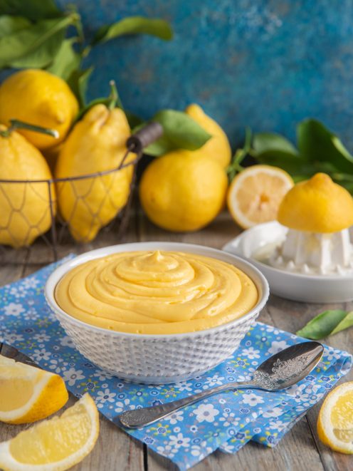 Crema pasticcera al limone vellutata in ciotola, circondata da limoni freschi e spicchi tagliati