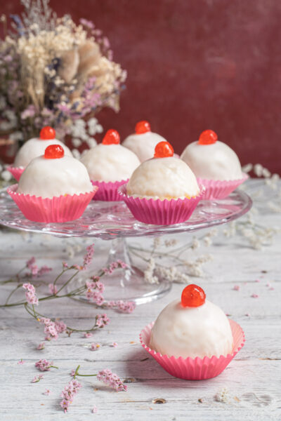 Dolci della sposa glassati di bianco con ciliegina candita sopra, serviti in pirottini rosa