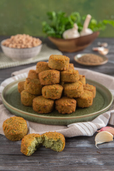 Falafel dorati e croccanti impilati a piramide, con uno spezzato che mostra l'interno verde