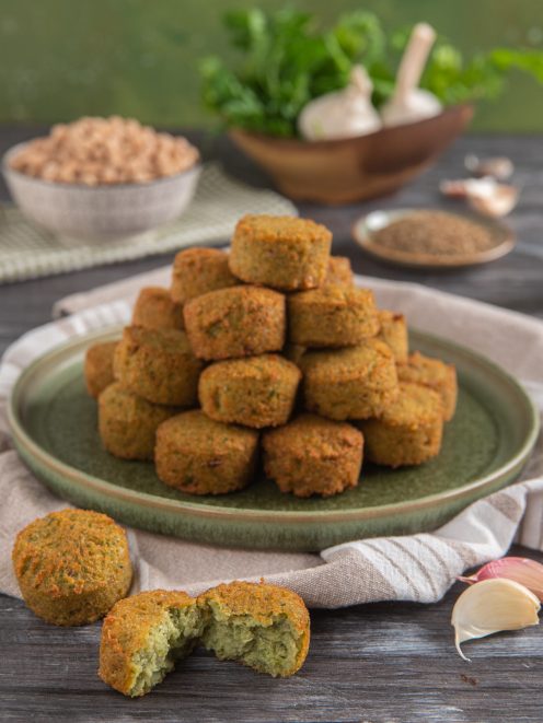 Falafel dorati e croccanti impilati a piramide, con uno spezzato che mostra l'interno verde