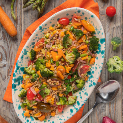 Insalata di farro con broccoli, pomodorini, carote e cipolla rossa servita su vassoio ovale