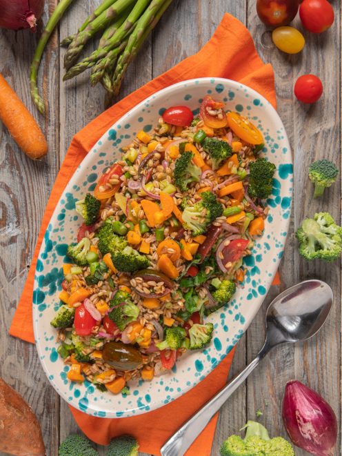 Insalata di farro con broccoli, pomodorini, carote e cipolla rossa servita su vassoio ovale