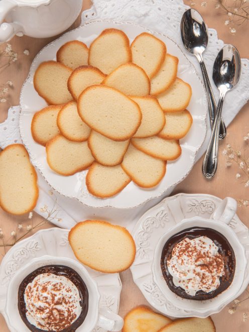 Lingue di gatto disposte a ventaglio, servite con coppette di crema al cioccolato e panna