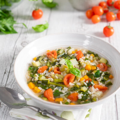 Minestrone di verdure con riso, pomodorini, zucchine e carote guarnito con basilico fresco