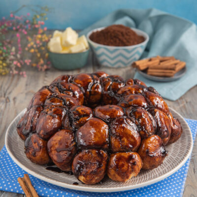 Monkey bread a palline glassate con caramello scuro, servito su un piatto con bastoncini di cannella
