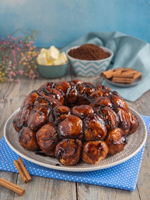 Monkey bread a palline glassate con caramello scuro, servito su un piatto con bastoncini di cannella