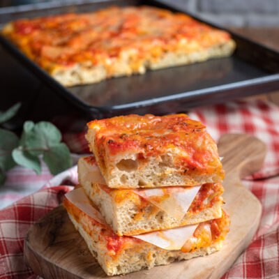 Pizza ad alta idratazione in teglia, con fette sovrapposte farcite con prosciutto e salsa di pomodoro