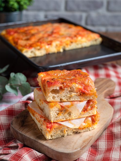 Pizza ad alta idratazione in teglia, con fette sovrapposte farcite con prosciutto e salsa di pomodoro