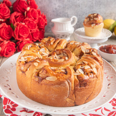 Torta delle rose soffice a forma di corona, glassata con marmellata e guarnita con lamelle di mandorle tostate