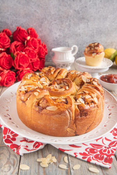 Torta delle rose soffice a forma di corona, glassata con marmellata e guarnita con lamelle di mandorle tostate