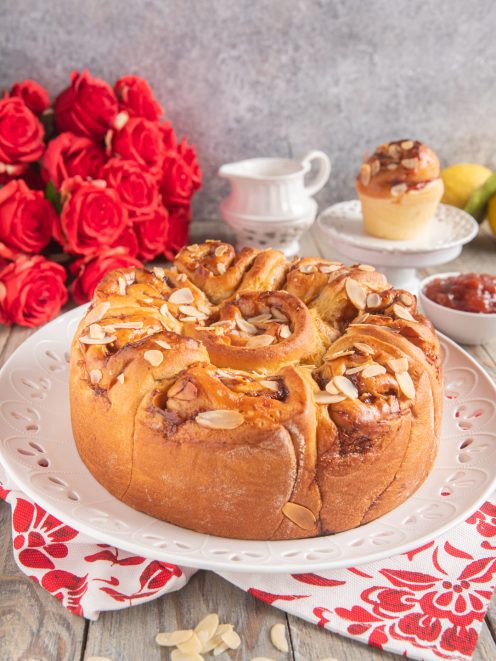 Torta delle rose soffice a forma di corona, glassata con marmellata e guarnita con lamelle di mandorle tostate
