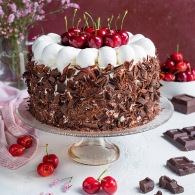 Torta foresta nera ricoperta di scaglie di cioccolato, con ciuffi di panna e ciliegie fresche in cima