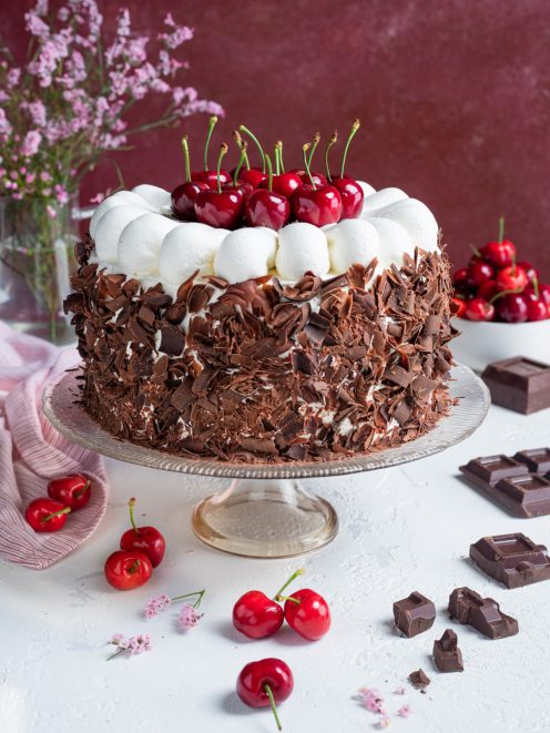 Torta foresta nera ricoperta di scaglie di cioccolato, con ciuffi di panna e ciliegie fresche in cima