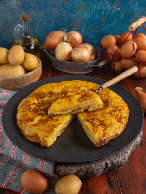Tortilla de patatas dorata con patate a strati, affettata e servita intera