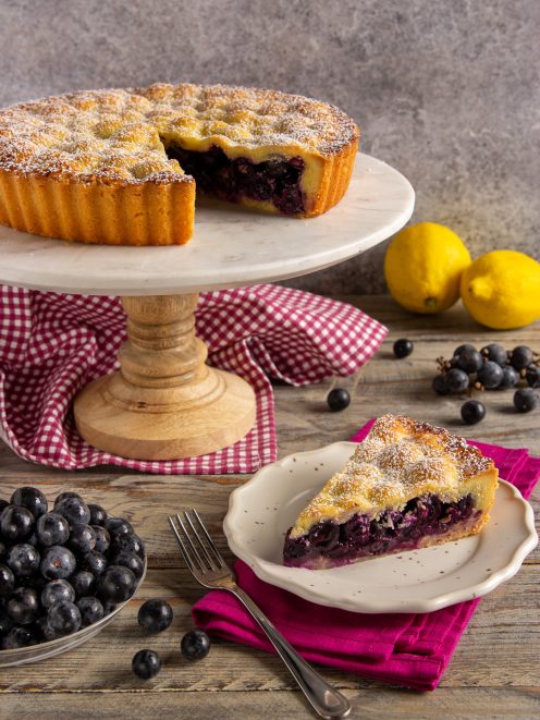 Crostata di uva fragola con una fetta servita al piatto, zucchero a velo in superficie