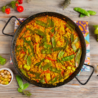 Paella Valenciana con riso allo zafferano, baccelli di fagiolini e pezzi di pollo nella padella da paella
