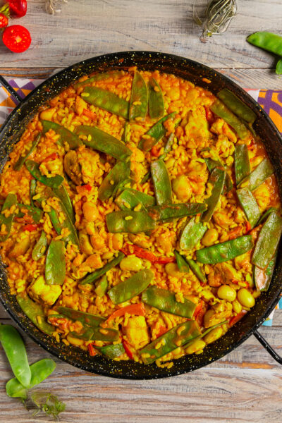 Paella Valenciana con riso allo zafferano, baccelli di fagiolini e pezzi di pollo nella padella da paella