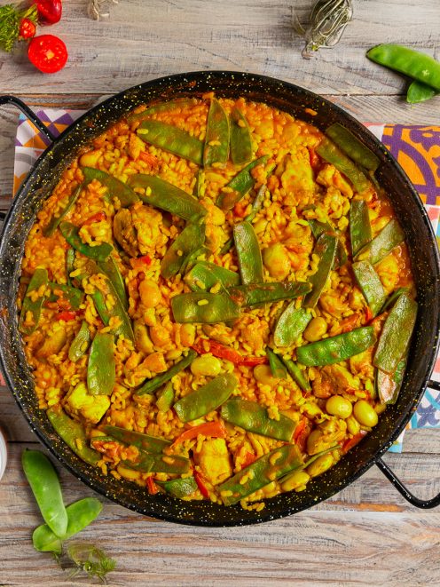 Paella Valenciana con riso allo zafferano, baccelli di fagiolini e pezzi di pollo nella padella da paella