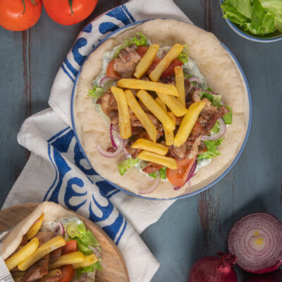 Pita gyros aperta con carne, patatine fritte, pomodoro, cipolla rossa e salsa tzatziki
