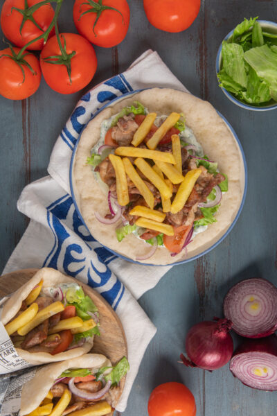 Pita gyros aperta con carne, patatine fritte, pomodoro, cipolla rossa e salsa tzatziki