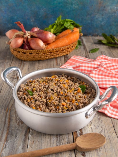 Ragù bianco con carne macinata, carote e cipolla tritata, guarnito con foglie di basilico