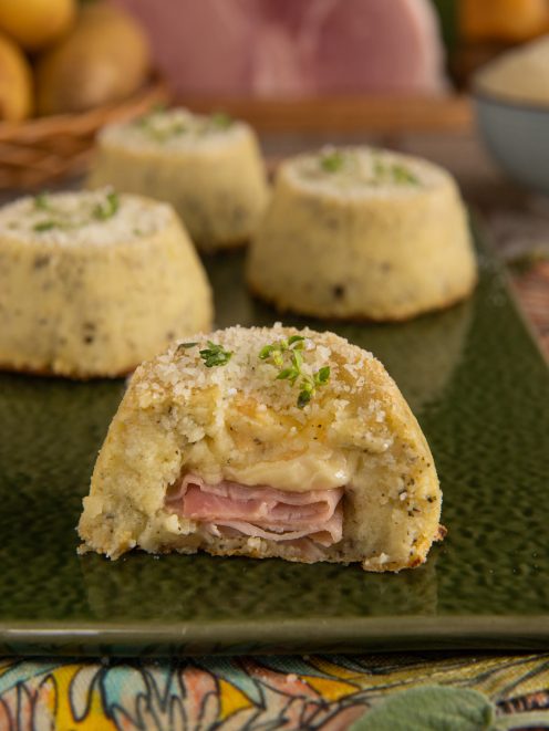 Tortino di patate tagliato a metà con ripieno di prosciutto cotto e formaggio filante, guarnito con erbe fresche