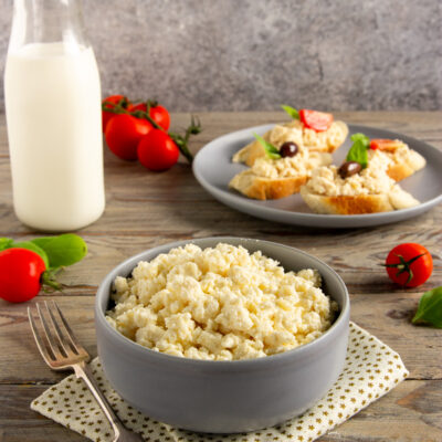 Fiocchi di latte freschi in una ciotola, con crostini guarniti di olive e basilico sullo sfondo