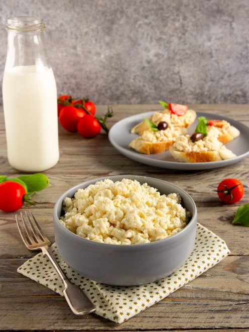 Fiocchi di latte freschi in una ciotola, con crostini guarniti di olive e basilico sullo sfondo