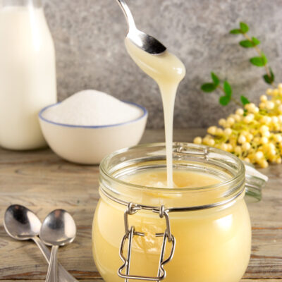 Latte condensato denso e cremoso versato con un cucchiaio in un barattolo di vetro