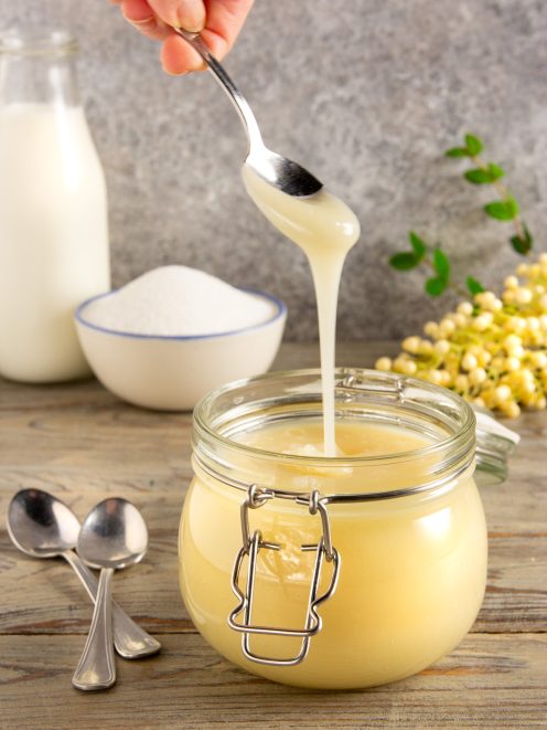 Latte condensato denso e cremoso versato con un cucchiaio in un barattolo di vetro