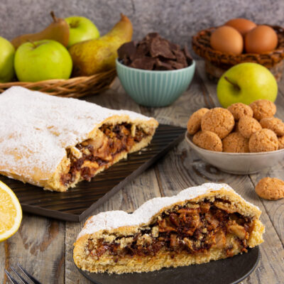 Strudel di frolla con mele, pere, cioccolato e noci tagliato a fetta, spolverato di zucchero a velo