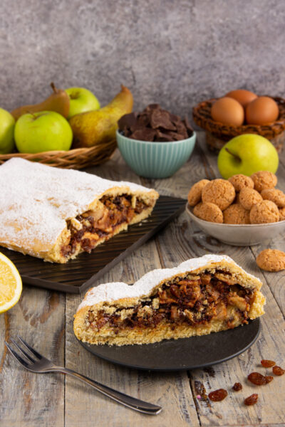 Strudel di frolla con mele, pere, cioccolato e noci tagliato a fetta, spolverato di zucchero a velo