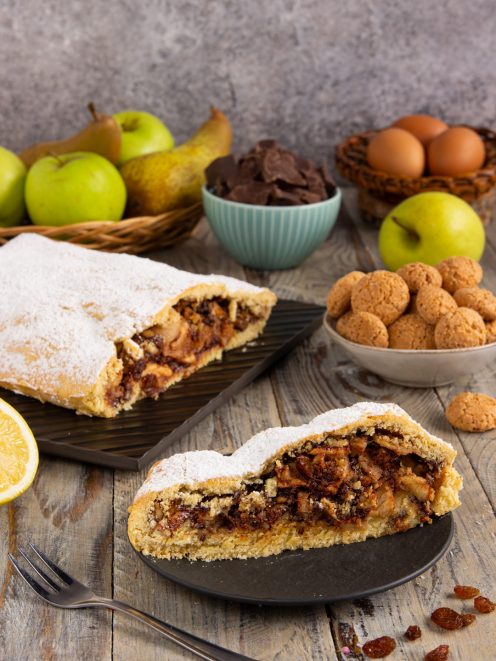 Strudel di frolla con mele, pere, cioccolato e noci tagliato a fetta, spolverato di zucchero a velo