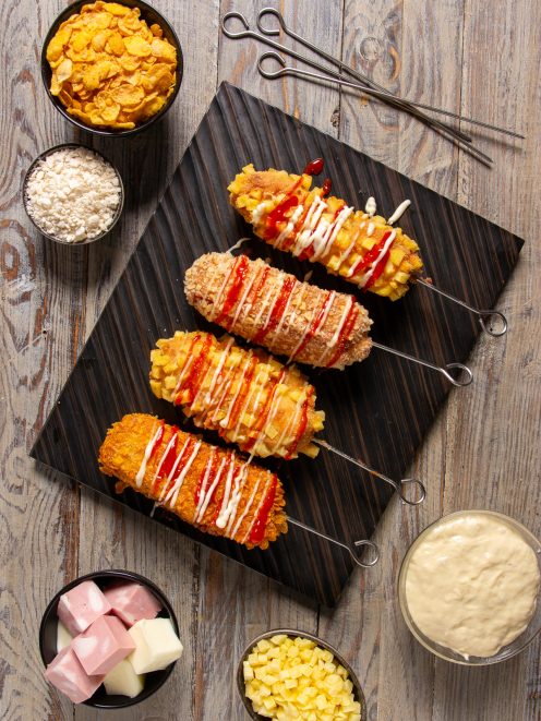 Korean corn dog fritti su spiedino con panature diverse, ketchup e maionese a filo