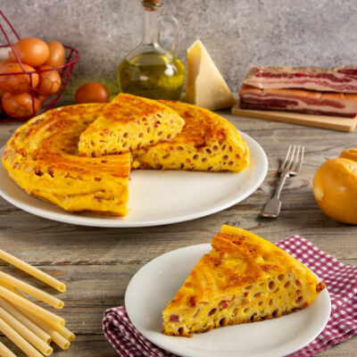 Frittata di pasta tagliata a fette con maccheroni, pancetta e uova ben visibili nella sezione