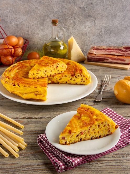 Frittata di pasta tagliata a fette con maccheroni, pancetta e uova ben visibili nella sezione
