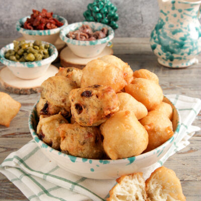 Pettole fritte dorate ammucchiate in una ciotola, alcune farcite con olive e pomodori secchi