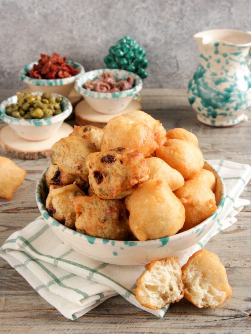 Pettole fritte dorate ammucchiate in una ciotola, alcune farcite con olive e pomodori secchi