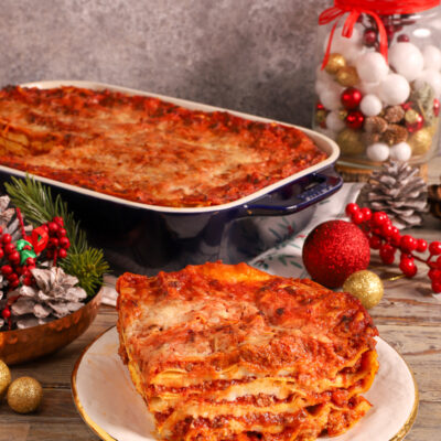 Lasagne delle Feste con strati di ragù e besciamella, servite a fetta con la teglia sullo sfondo