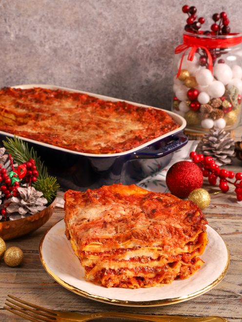Lasagne delle Feste con strati di ragù e besciamella, servite a fetta con la teglia sullo sfondo