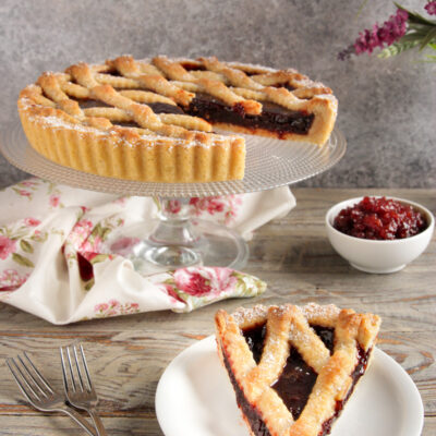 Crostata con frolla senza uova ricoperta di grigliato e confettura, con una fetta servita a parte