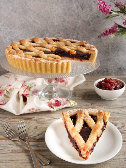 Crostata con frolla senza uova ricoperta di grigliato e confettura, con una fetta servita a parte