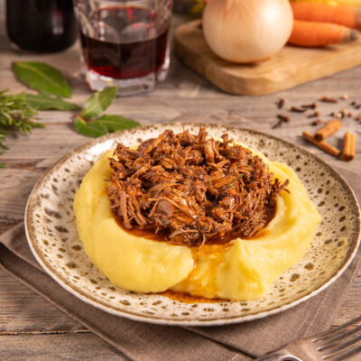 Stracotto di manzo sfilacciato con sugo scuro servito su letto di purè di patate